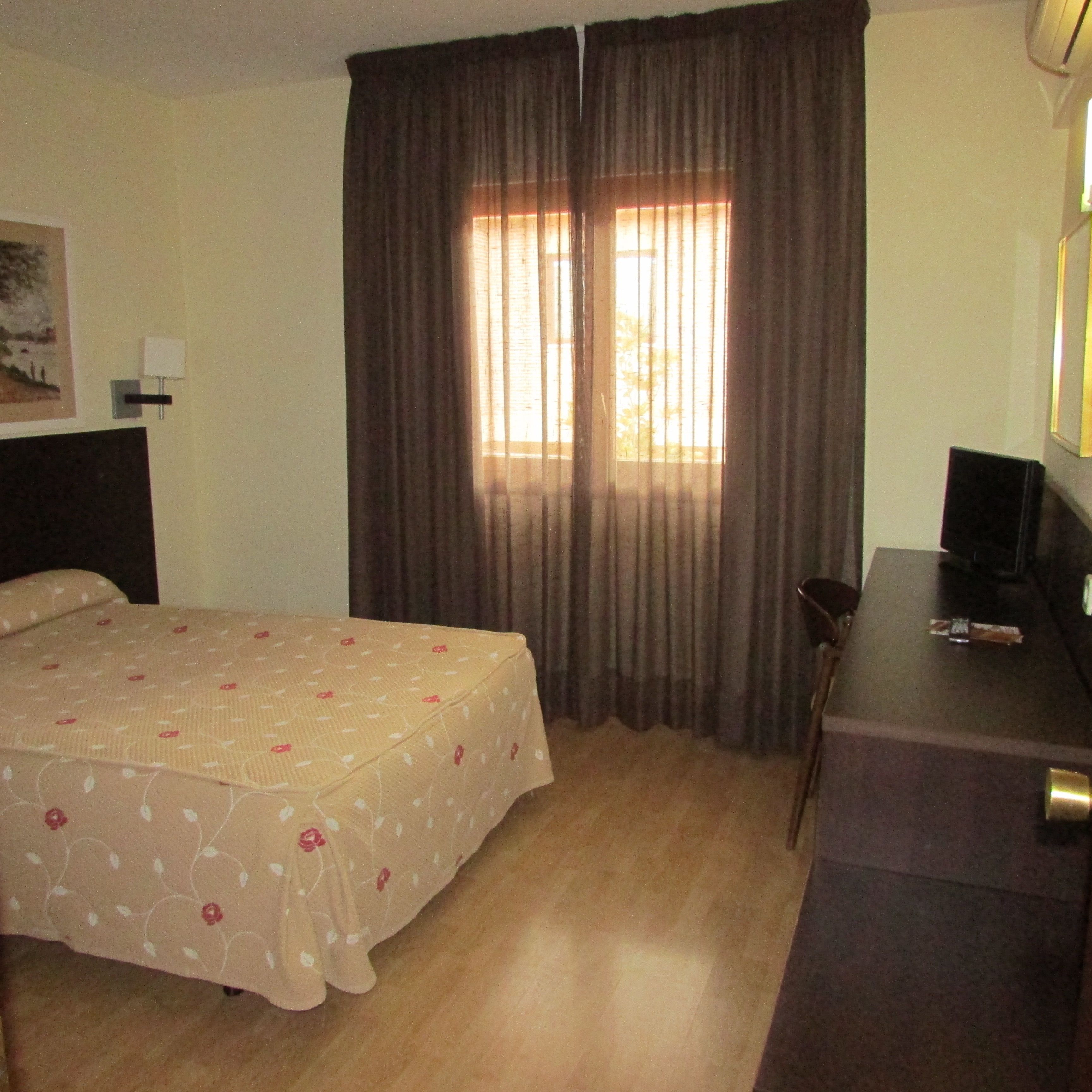 Une chambre d’hôtel avec un lit, un bureau et une fenêtre avec des rideaux.