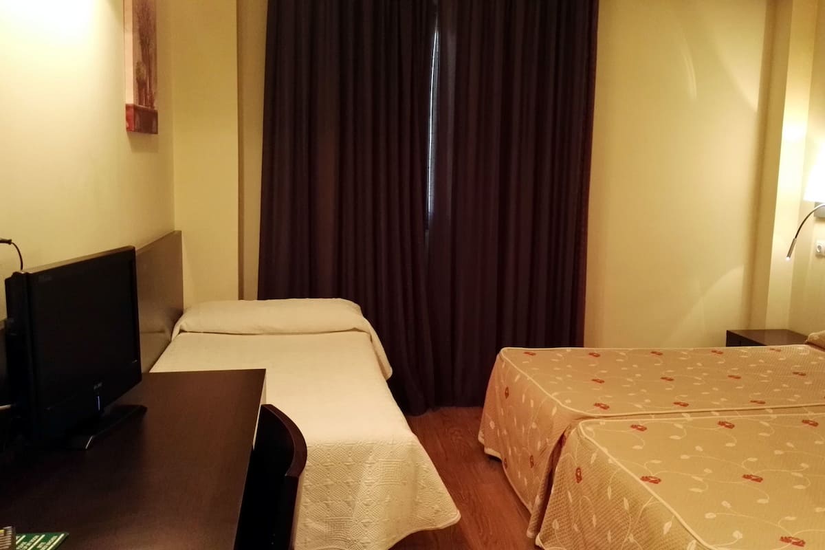 A hotel room with two beds, a desk with a television, and a window with curtains.
