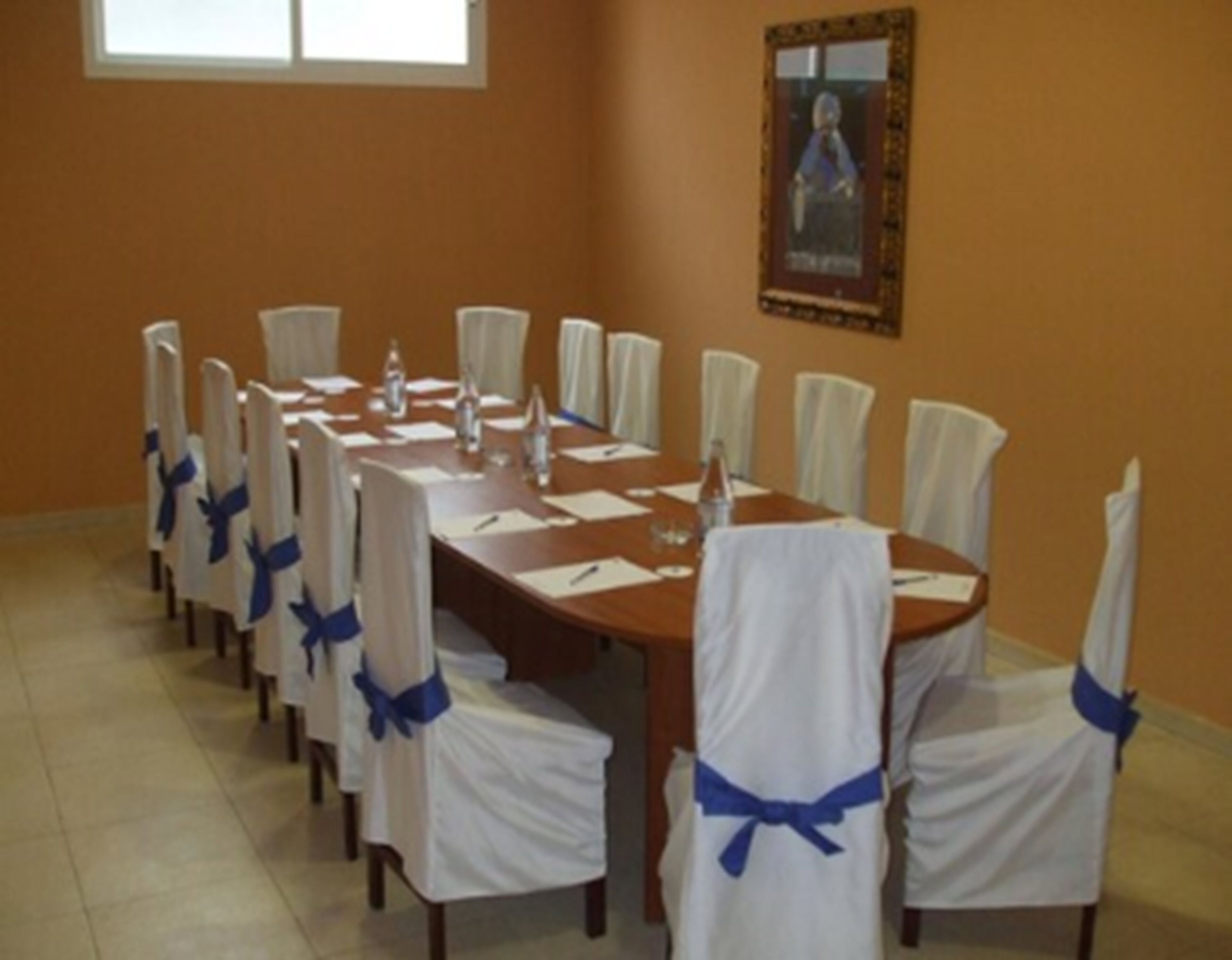 A conference room with a long table, chairs with blue sashes, and a poster on the wall.