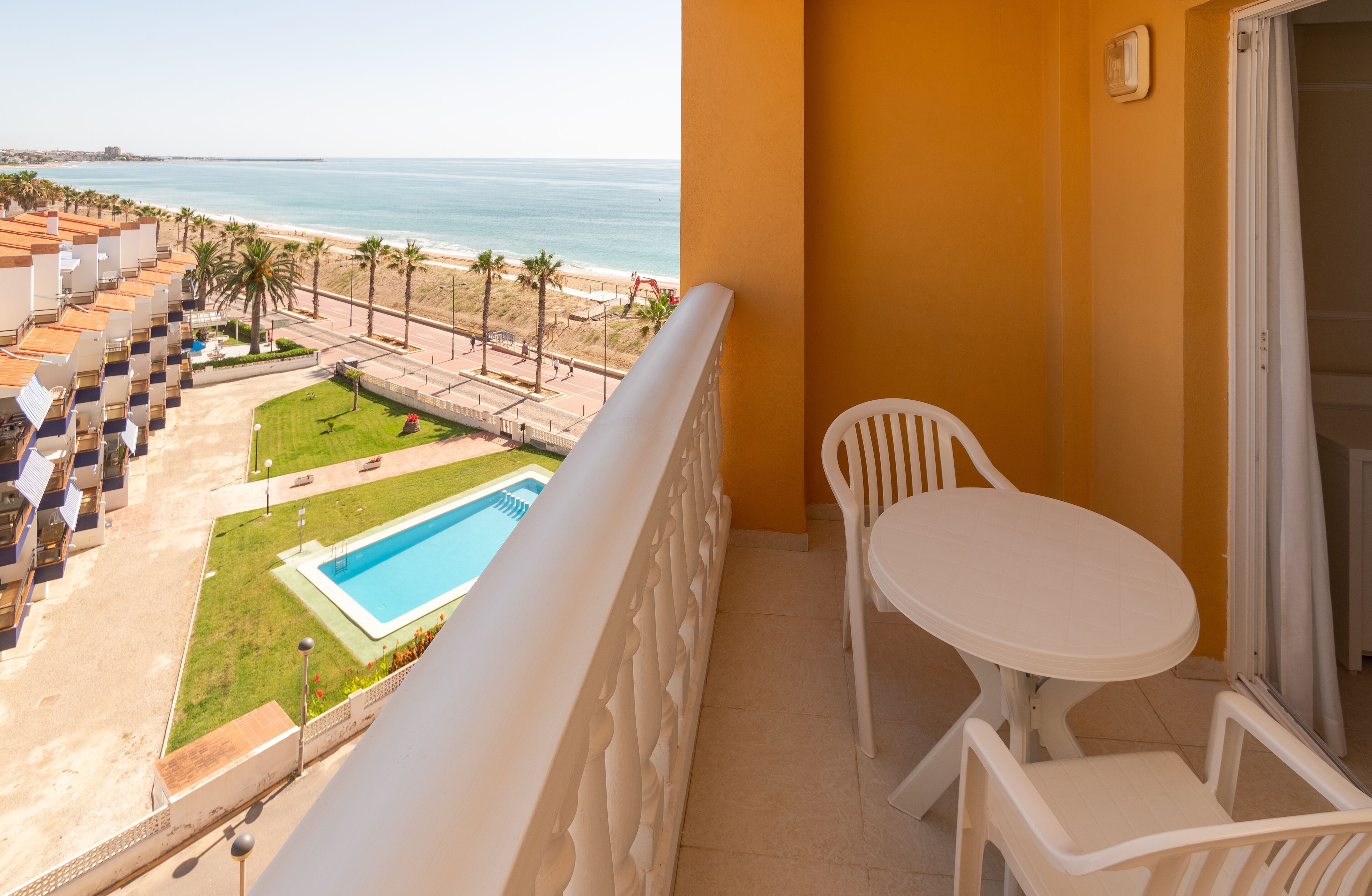 A balcony with a pool, chairs, and a view of the beach and ocean.