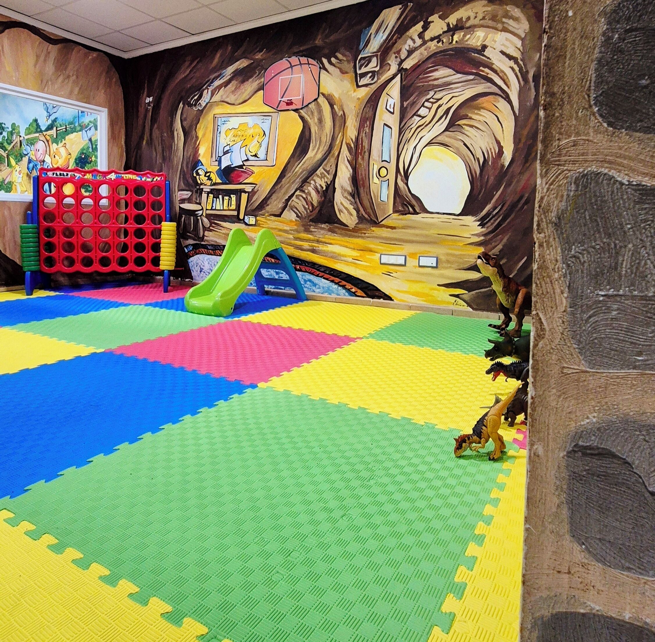 A play area with a colorful floor, a slide, and a mural.