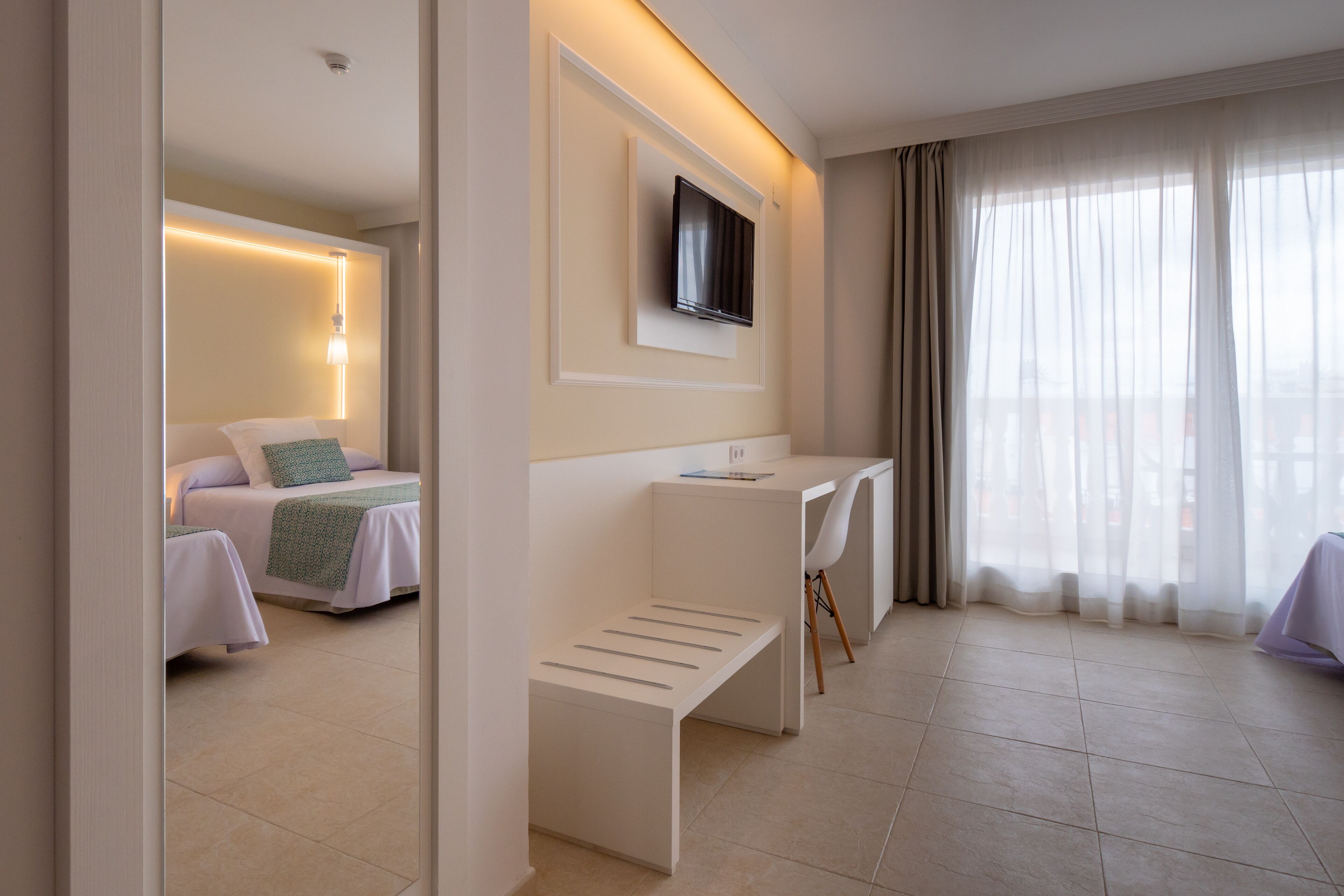 A modern hotel room with a bed, a desk, and a TV mounted on the wall.