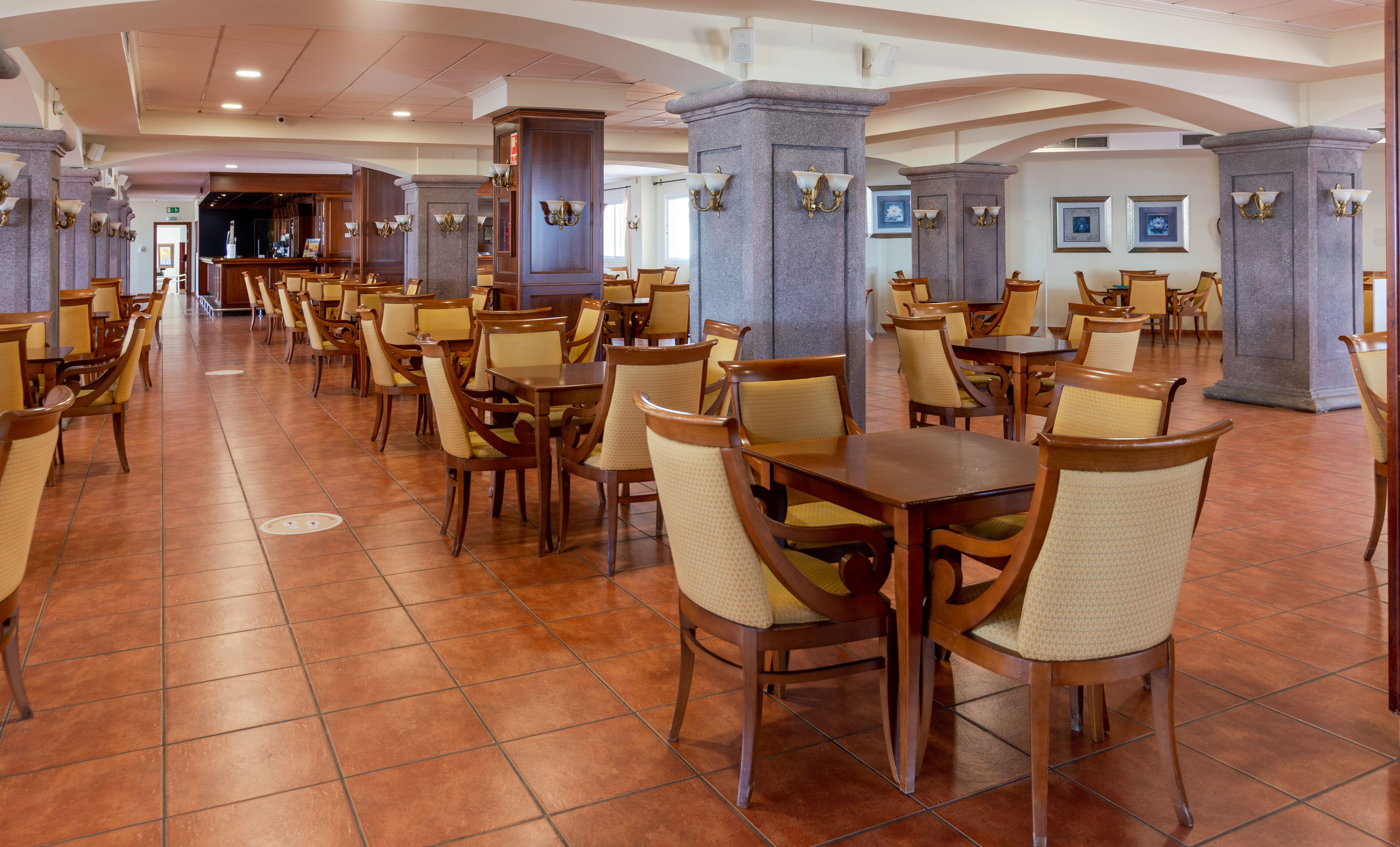 Un vaste espace dédié à la salle à manger, avec de nombreuses tables et chaises, agrémenté de piliers en pierre et d’un éclairage mural.