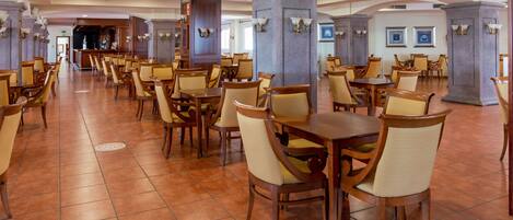 A spacious dining area with multiple tables and chairs, featuring stone pillars and wall-mounted lighting.
