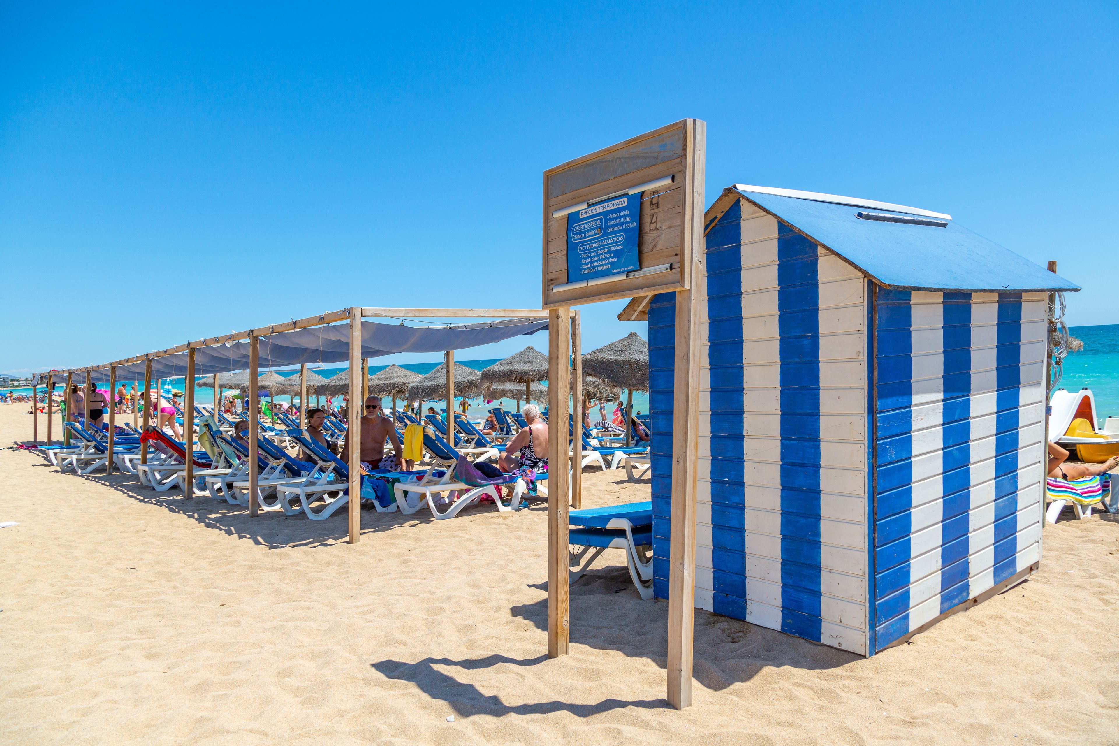 Una playa con tumbonas y una cabaña de playa a rayas.