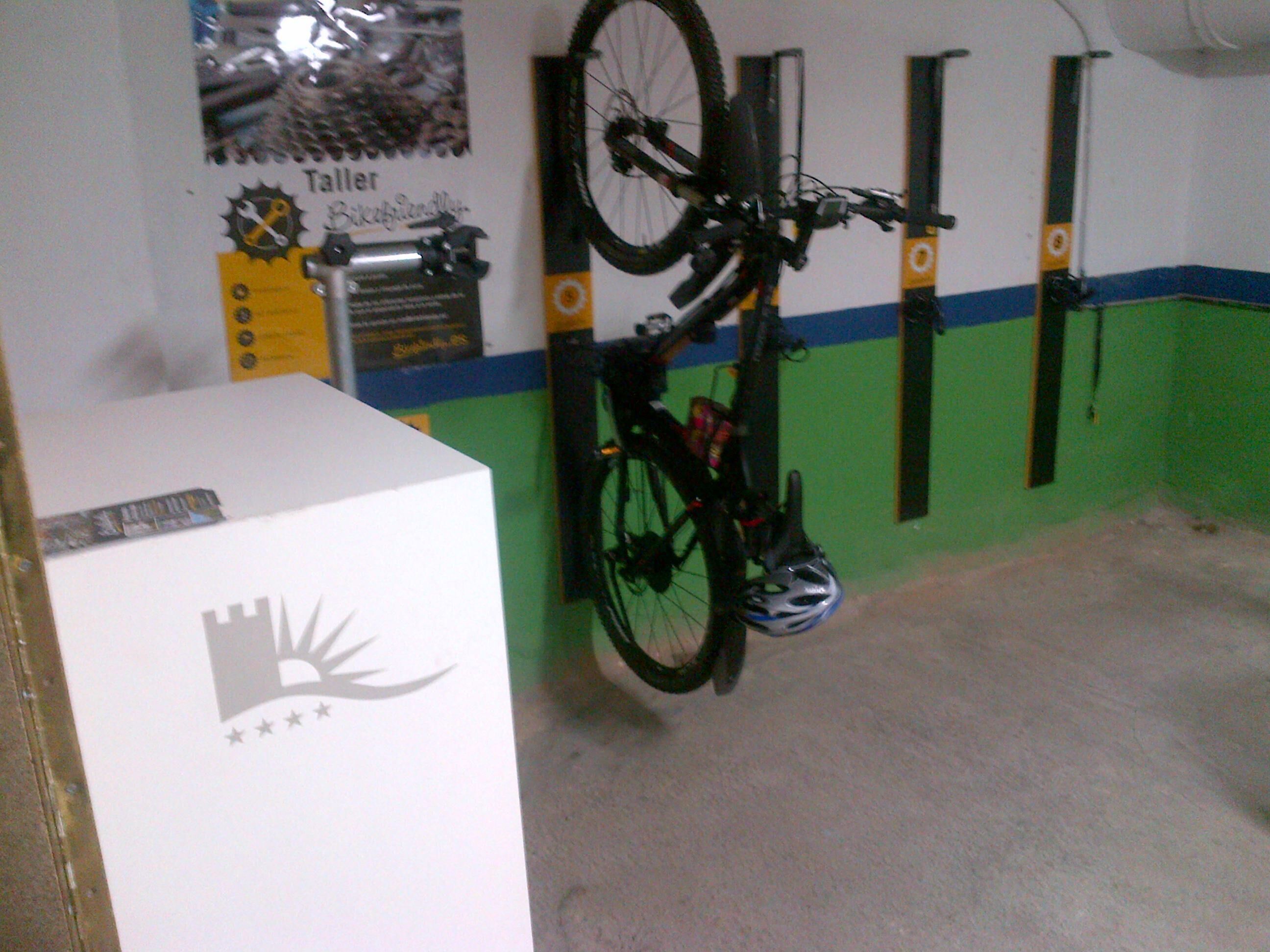 A room with a bicycle mounted on a wall, a white box with a logo, and a green and blue wall.