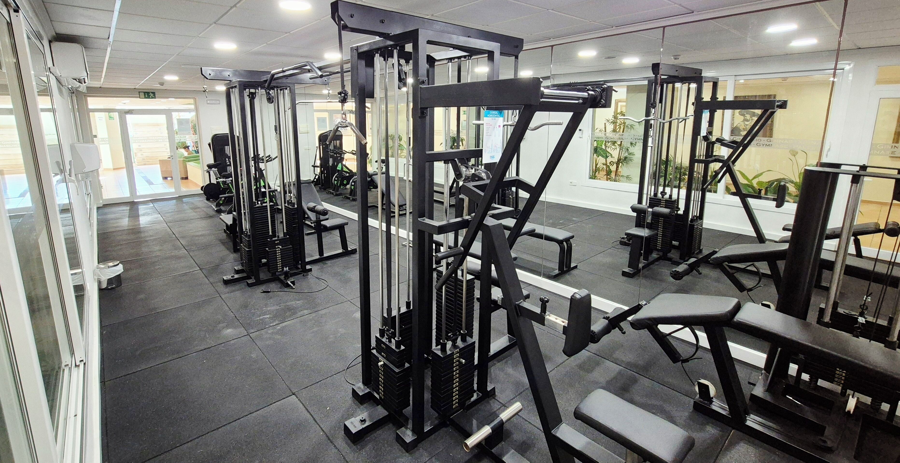 Ein Fitnessraum mit verschiedenen Trainingsgeräten, einer Rezeption und Blick ins Freie.