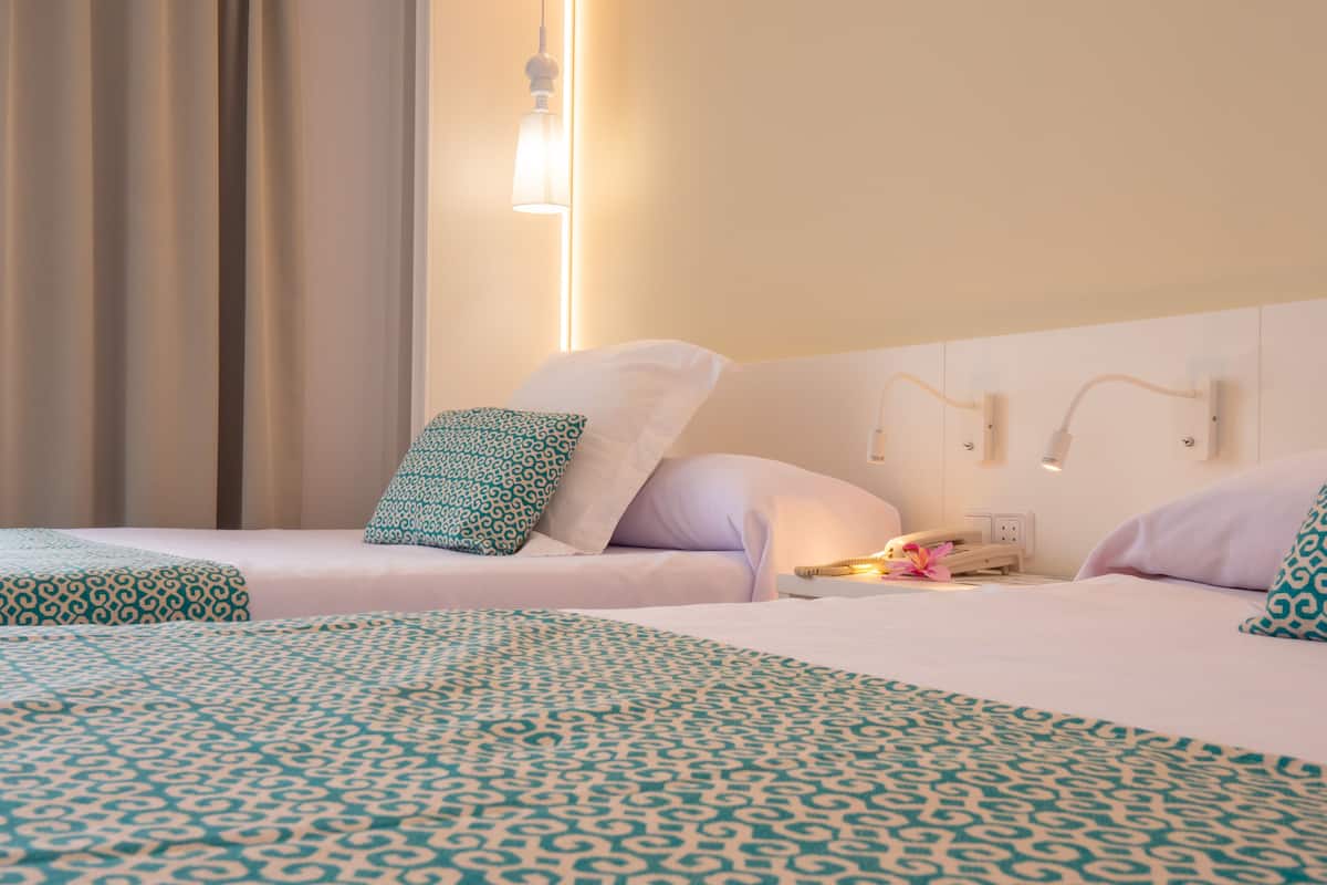 Une chambre d’hôtel avec deux lits, chacun agrémenté de draps à motifs, une table de chevet avec une lampe et un luminaire fixé au mur.
