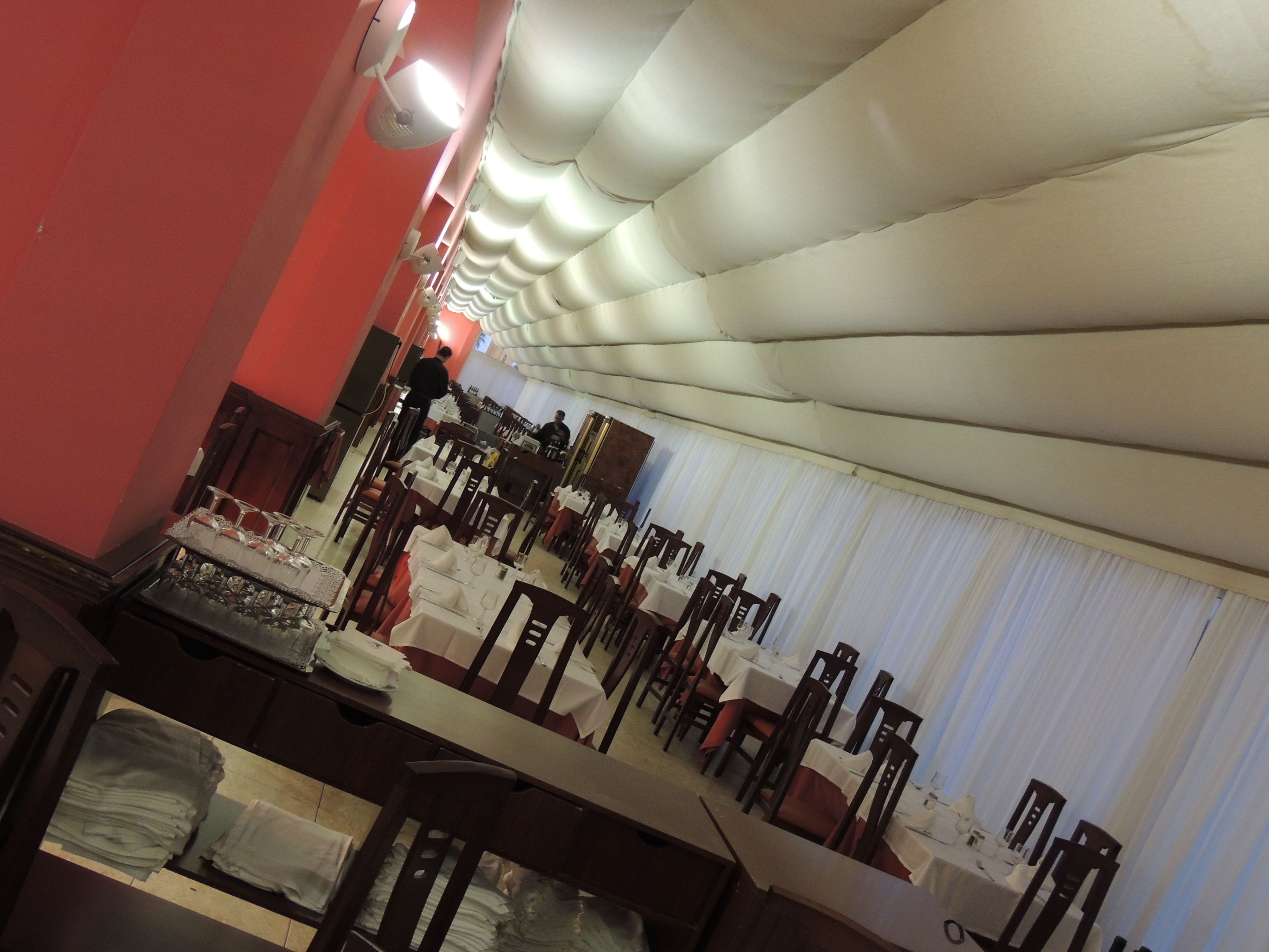 Un salón de banquetes con mesas dispuestas para un evento formal, un escenario con un atril y un techo de diseño único.
