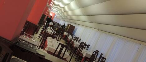 Un salón de banquetes con mesas dispuestas para un evento formal, un escenario con un atril y un techo de diseño único.