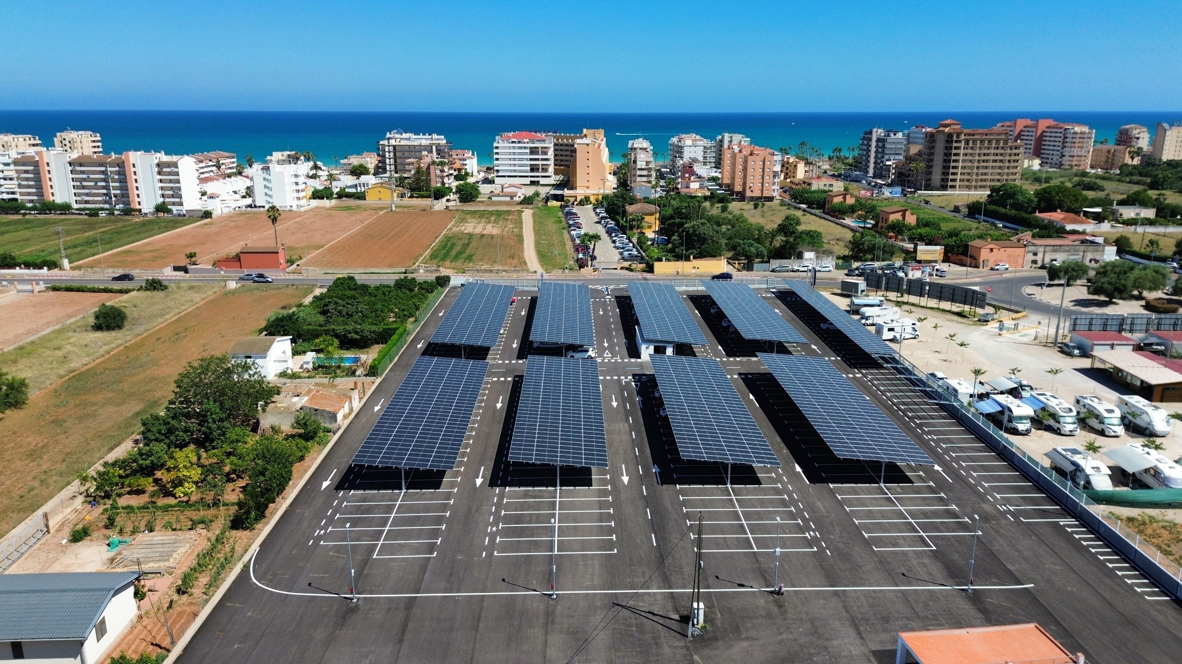 A parking lot with solar panels, a road, and buildings in the background.