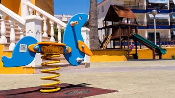 A playground with a blue and yellow seesaw and a slide.