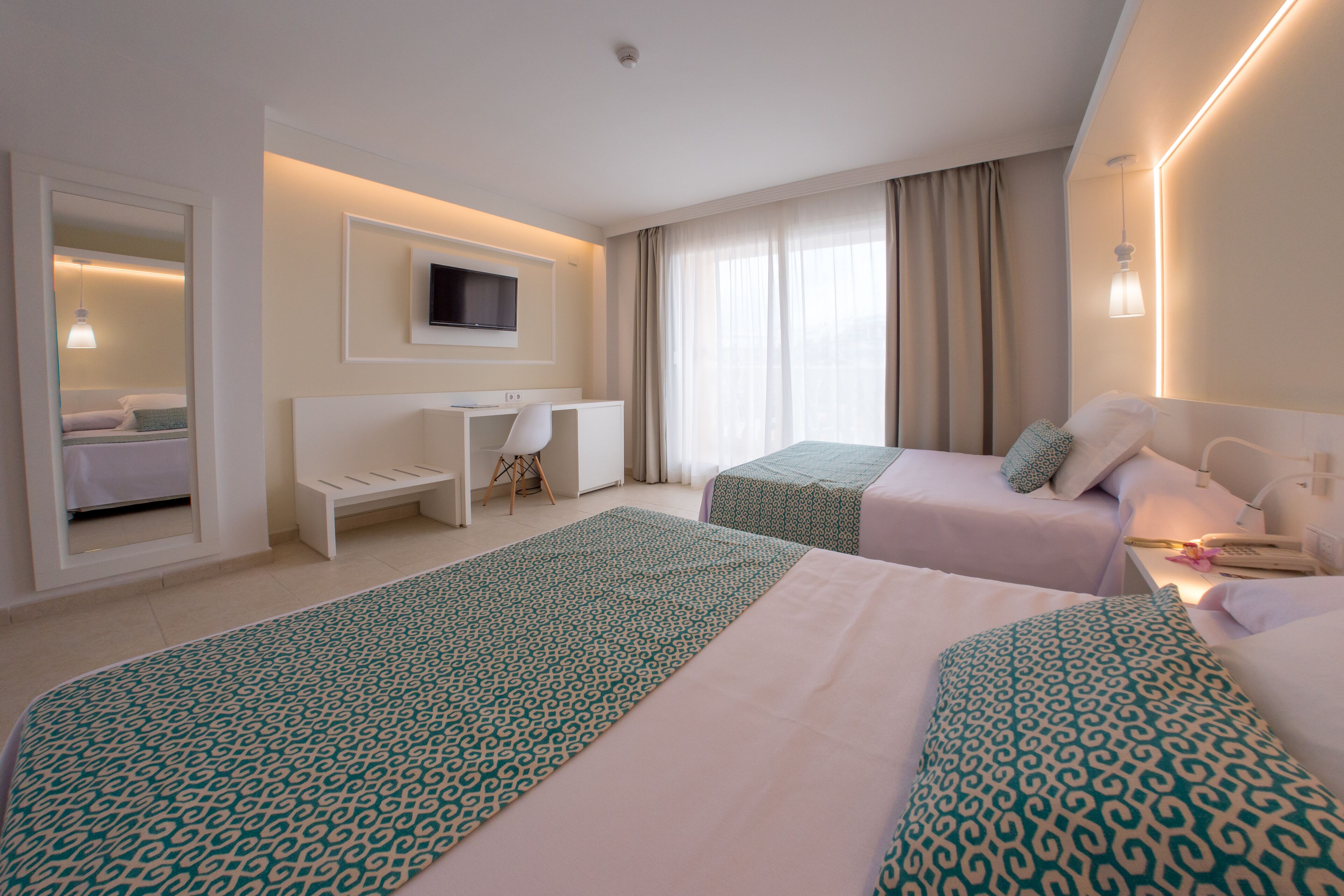 A hotel room with two beds, a desk, a TV, and a window with curtains.