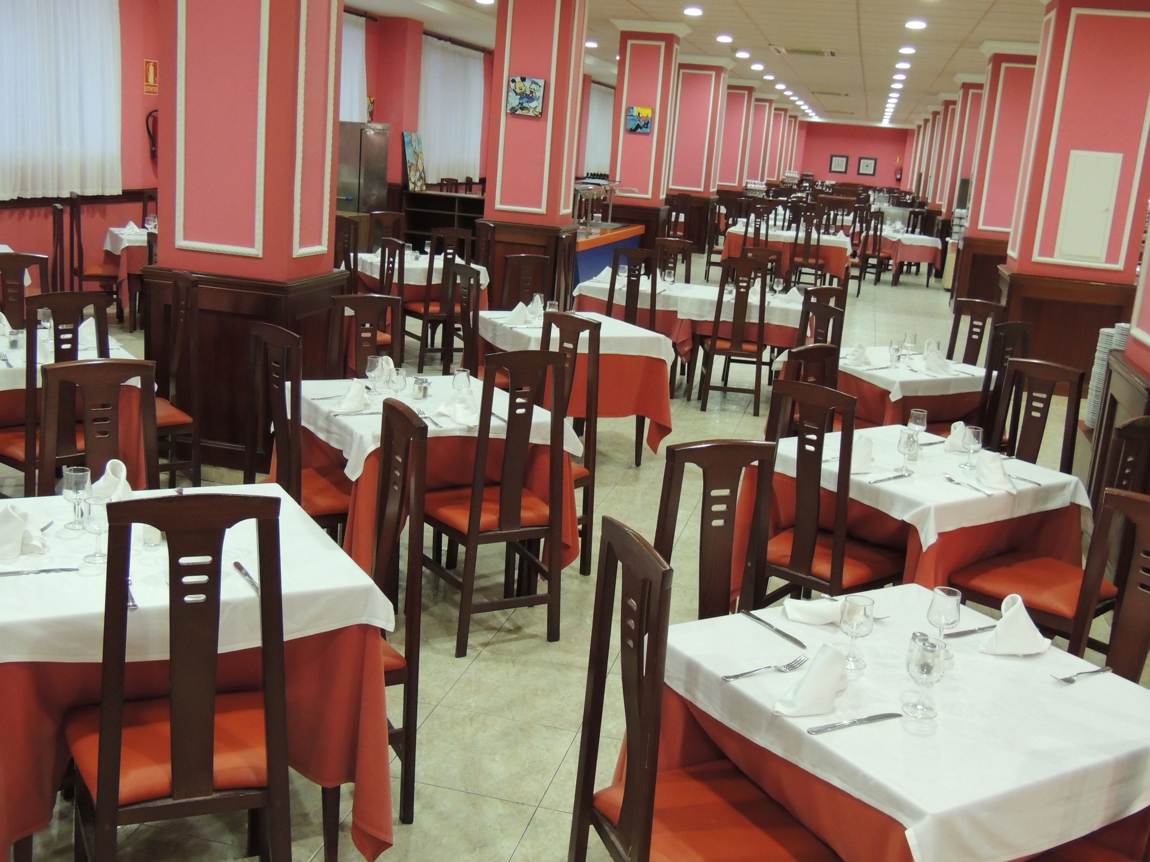 En restaurant med flere borde og stole, dækket med hvide duge og bestik.