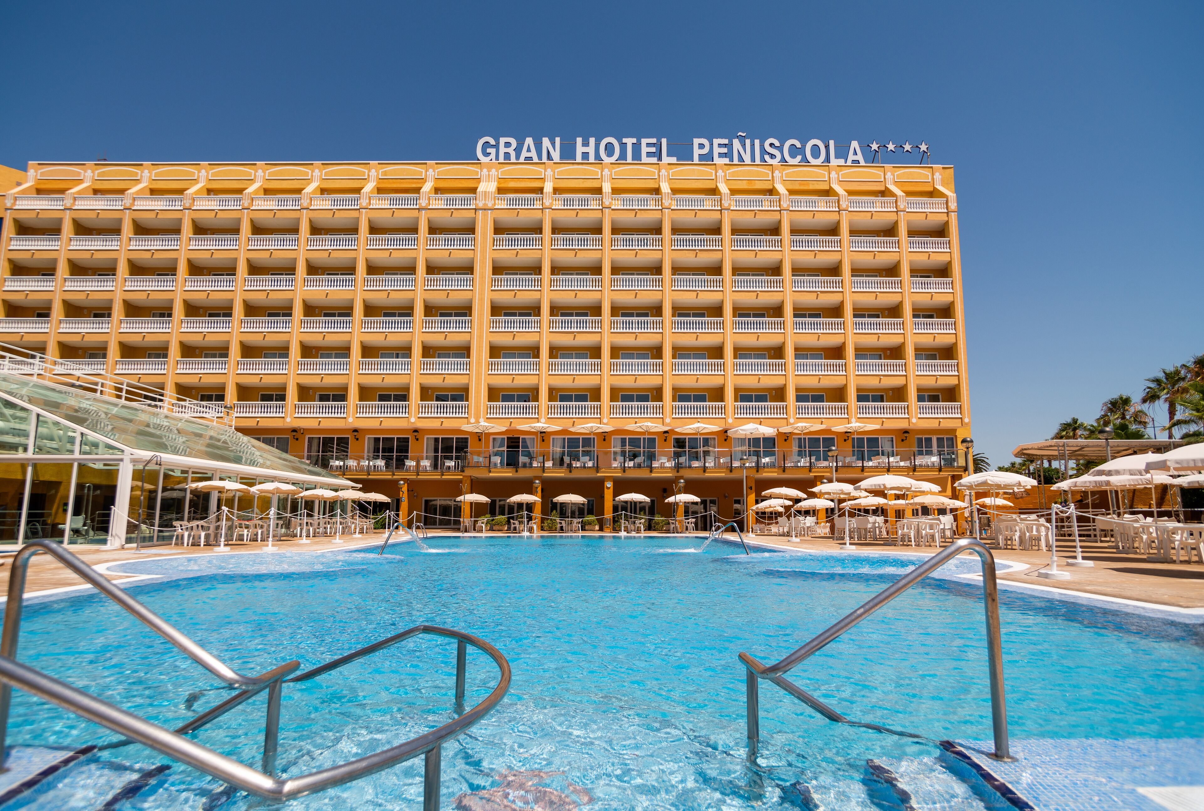 Et hotel med en stor pool, flere altaner og parasoller.