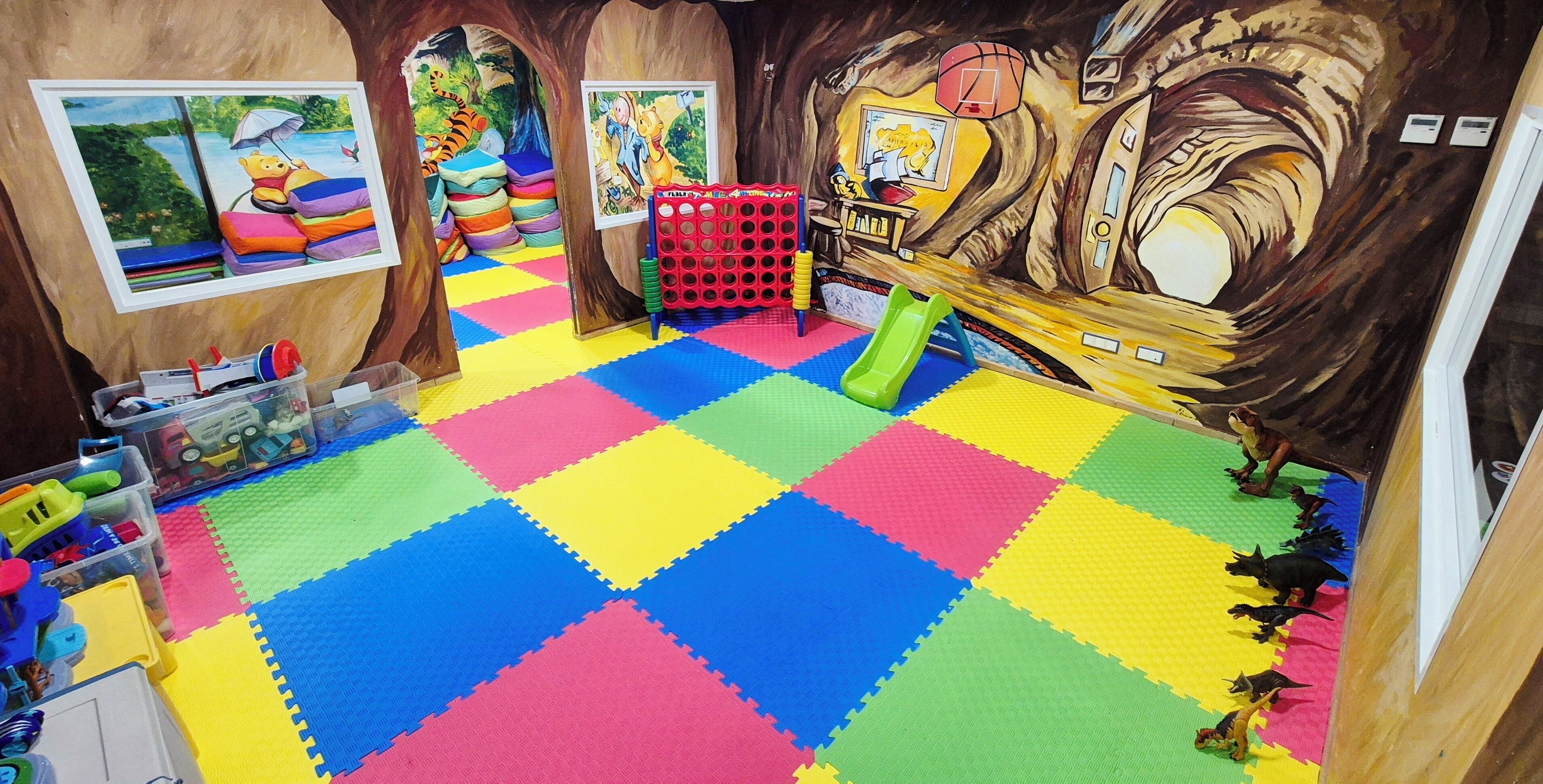Una sala de juegos con coloridos tapetes de espuma, juguetes y un mural.