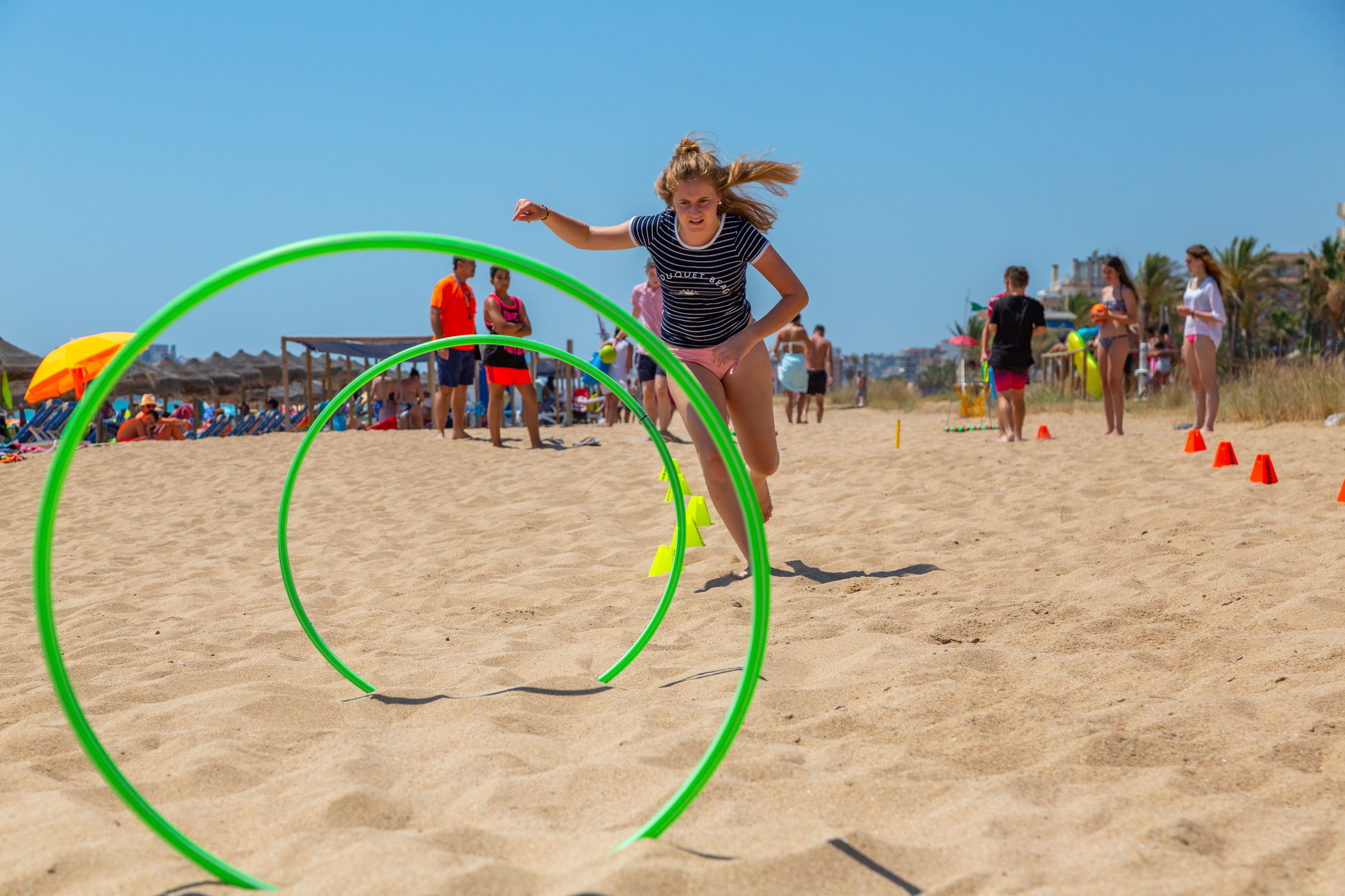 A beach with people, including a woman running through green hoops.