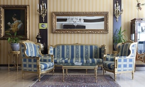 A room with a blue and gold patterned sofa set, a chandelier, and a large mirror on the wall.