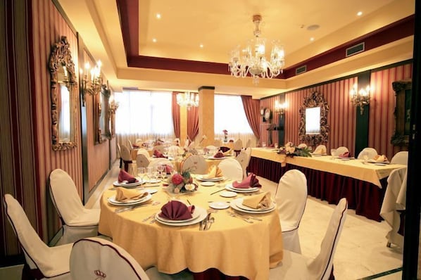 A banquet hall with round tables set for a formal event, featuring chandeliers and ornate wall decorations.