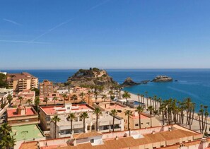 A coastal town with buildings, palm trees, and a rocky outcrop in the background.