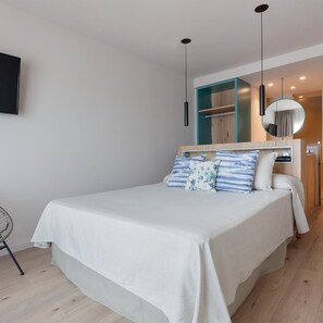 Un dormitorio moderno con cama, mesita de noche y televisor fijado a la pared.