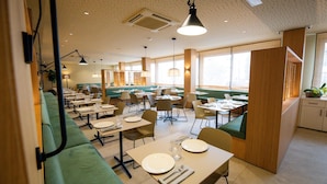 A modern dining area with green seating, multiple tables, and pendant lighting. - Maritim (Roses)