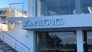 A building with a sign reading 'Les ALGUES' and a glass facade reflecting outdoor scenery. - Maritim (Roses)