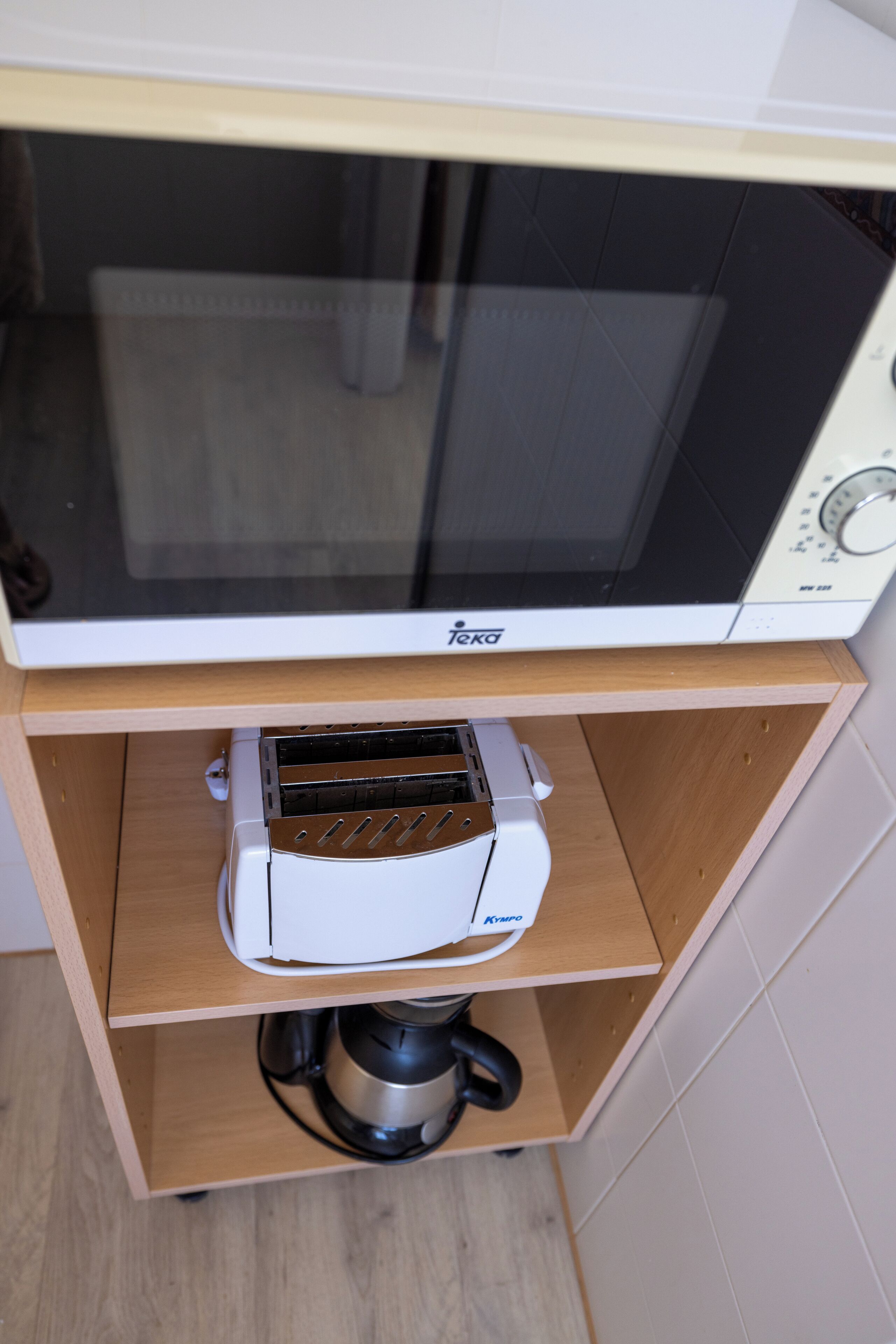 A microwave oven on a wooden shelf above a toaster.