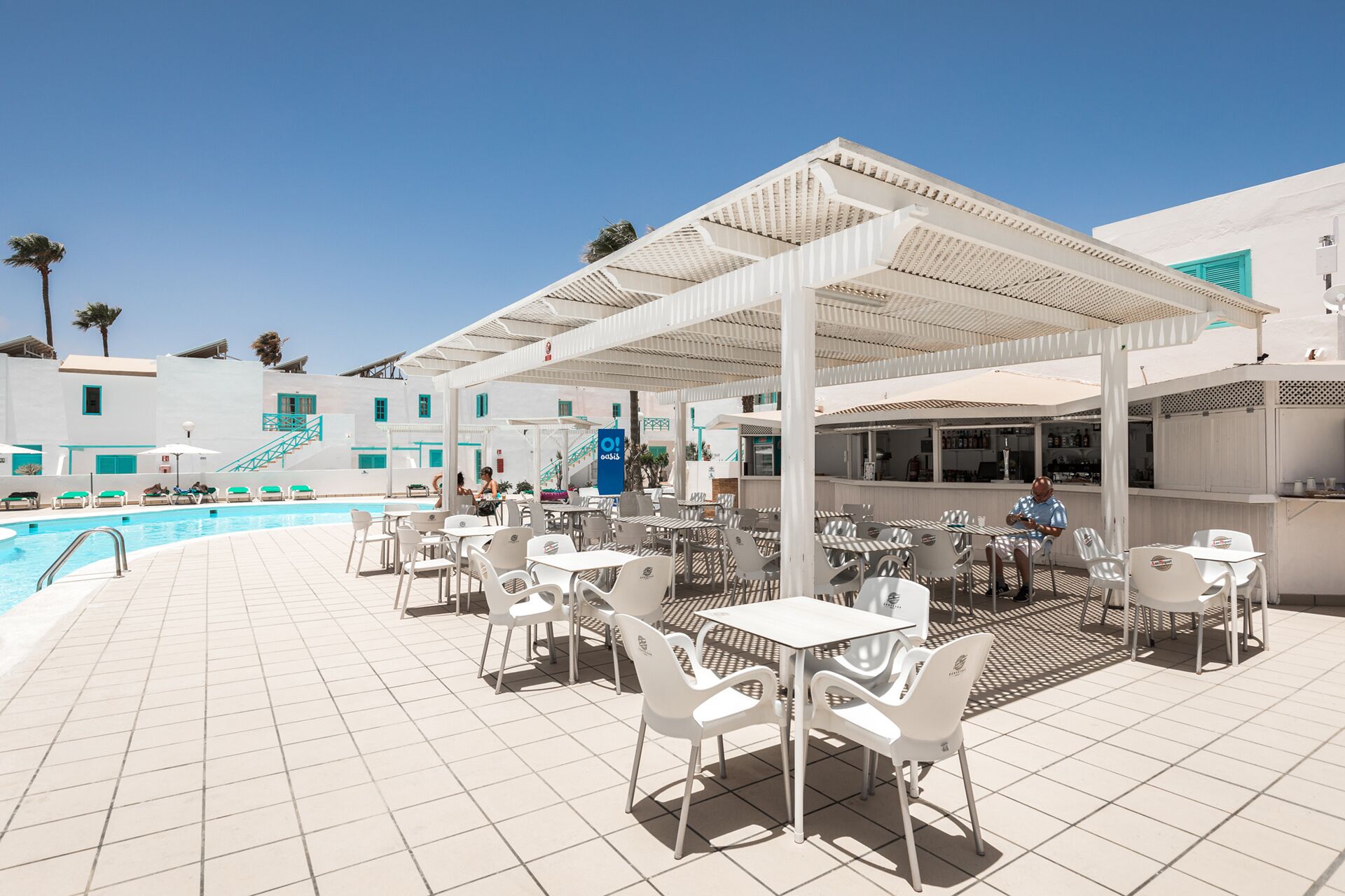Zona junto a la piscina con asientos al aire libre y un bar.