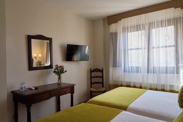A hotel room with two beds, a TV, a mirror, a desk with a vase of flowers, and a chair.