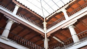 Un patio con escalera de madera, una fuente blanca y un área de comedor con sillas y una mesa.