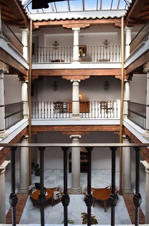Un patio de varios niveles con un espacio abierto central, columnas y un balcón con barandilla.