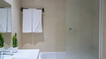 Un baño con lavamanos blanco, ducha con cerramiento de vidrio y una planta en maceta.