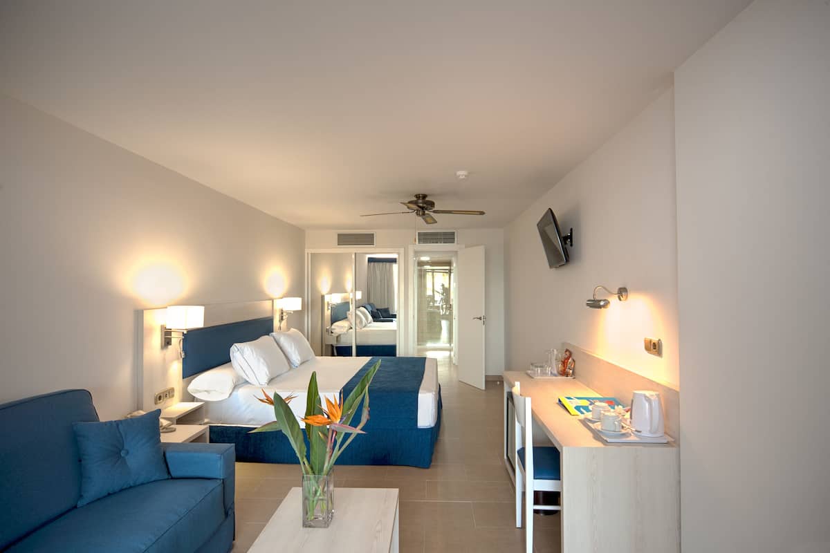 A hotel room with a bed, a sofa, a desk, and a TV.