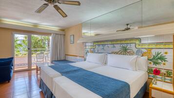Una habitación de hotel con una cama grande, una cama más pequeña, un balcón con una silla y un ventilador de techo.