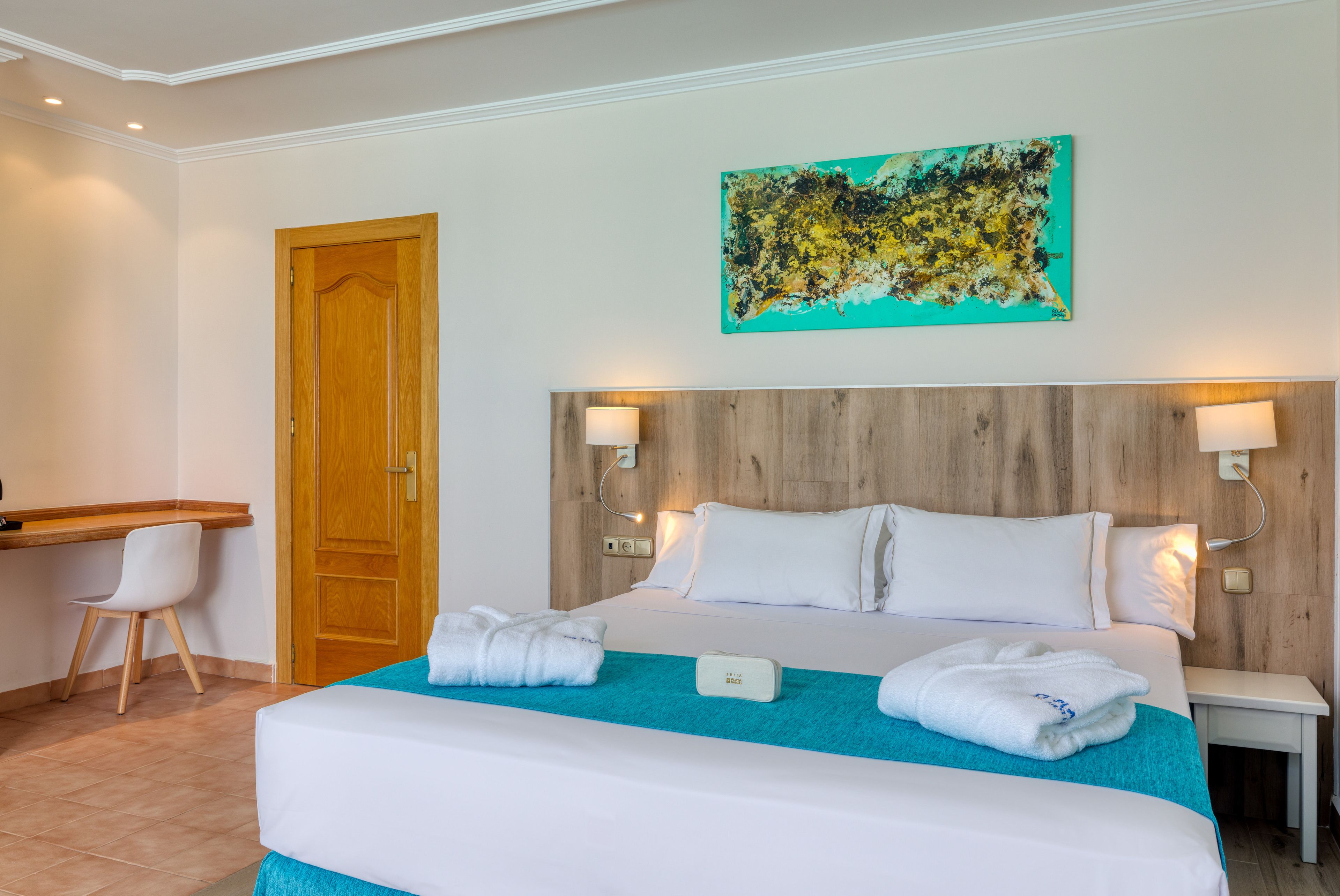 A hotel room with a wooden headboard, a desk with a chair, and a bed with white bedding and towels.