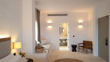 Habitación de hotel con cama, sofá, sillón, mesita, lámpara y puerta.