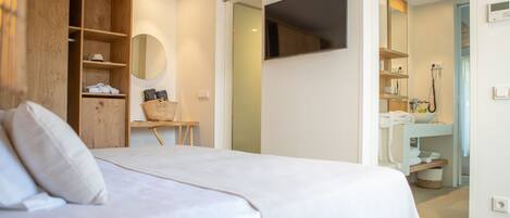 A bedroom with a bed, a wooden wardrobe, a small table with a basket, and a bathroom visible through an open door.