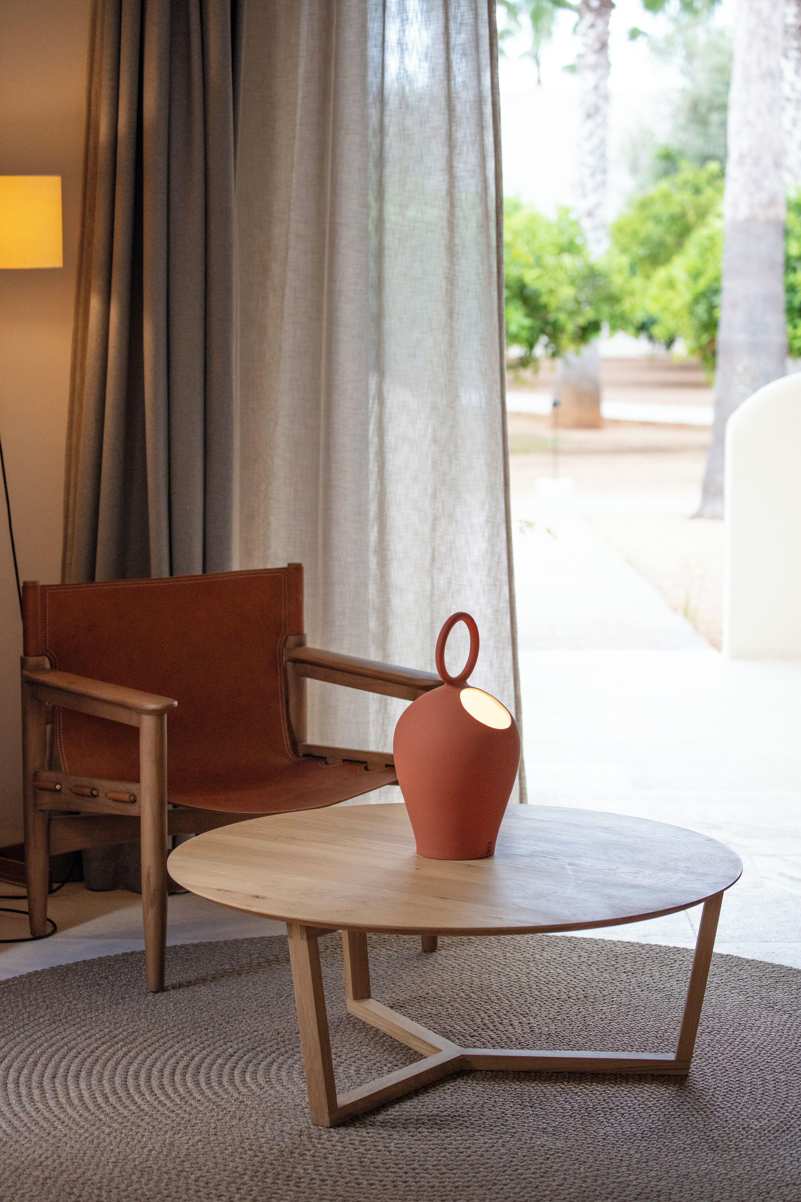 Una habitación con una mesa redonda, una silla, una lámpara y vistas a espacios verdes.