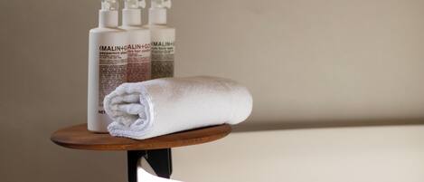 A bathroom with a white towel on a wooden stool, a bottle of shampoo, and a bottle of conditioner.