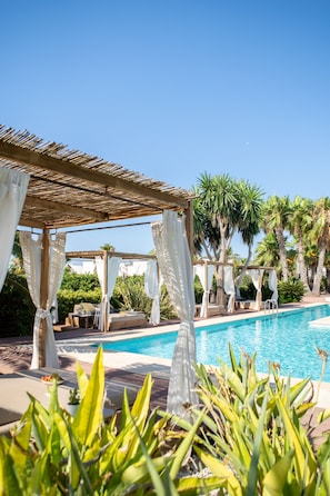 Un área de piscina con una pérgola, sillones de descanso y un cielo azul despejado.