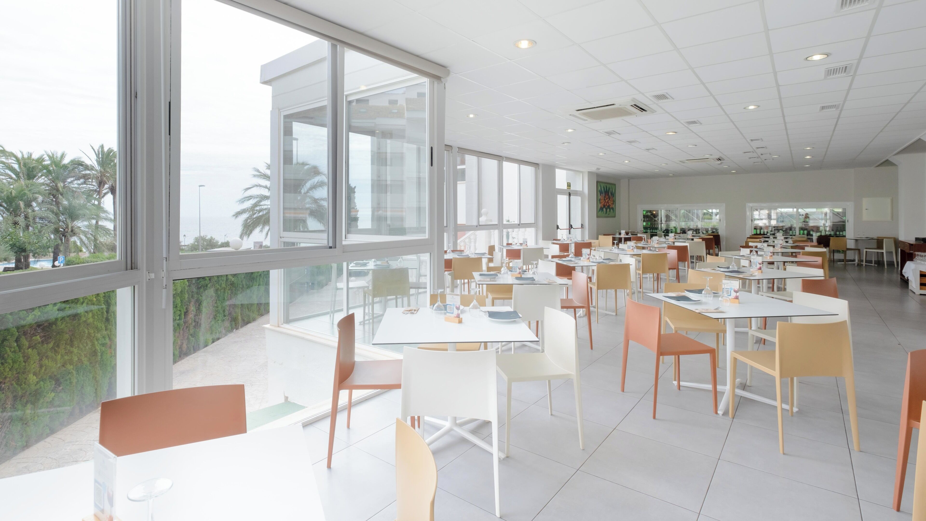 A spacious dining area with large windows, white tables, and chairs.
