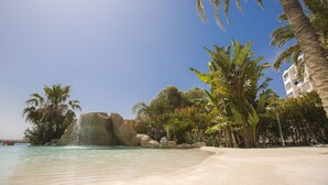 A beach with clear water, palm trees, and a rocky outcrop. - GRAN HOTEL LAS FUENTES (Alcala de Xivert)