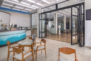 Zona de bar moderna con una mesa de vidrio y sillas de madera, una barra con diferentes botellas y vistas a un comedor con una escalera.