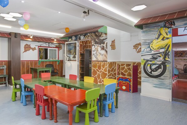 Un espacio interior muy colorido con una mesa larga y varias sillas, un mural en la pared e iluminación empotrada en el techo.