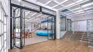 A modern lobby with a glass door entrance, a reception desk, and a staircase leading to upper floors. - GRAN HOTEL LAS FUENTES (Alcala de Xivert)