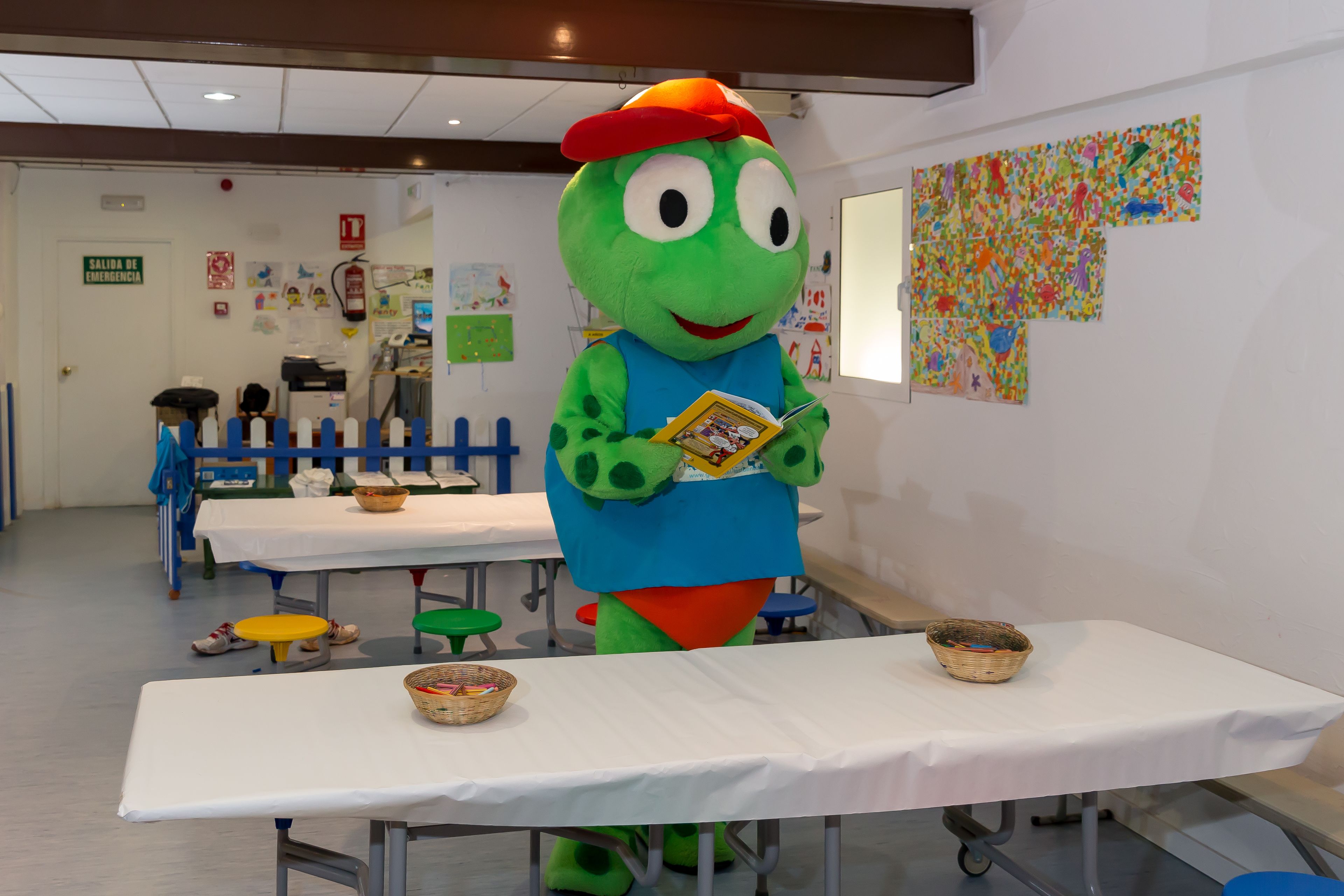 A room with a table, chairs, and a mascot holding a book.