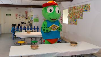 A room with a table, chairs, and a mascot holding a book.