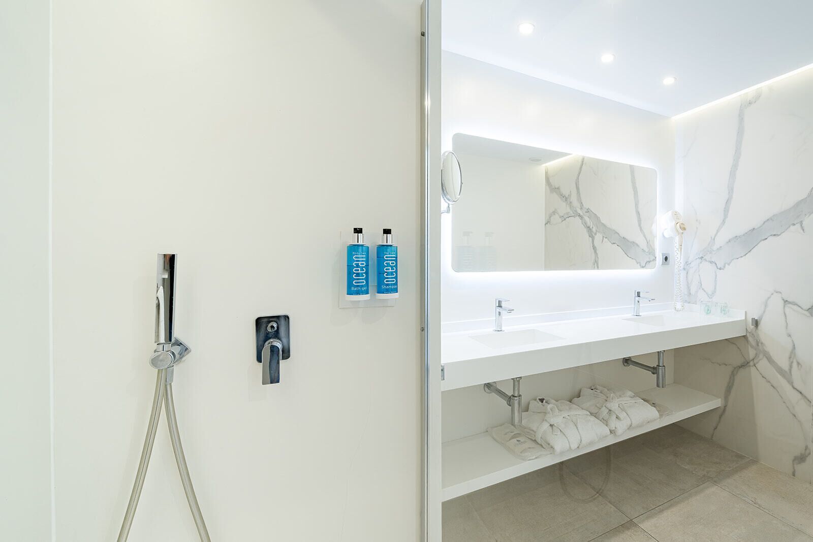Une salle de bain moderne équipée d’une douche, de deux lavabos, d’un grand miroir et d’un porte-serviettes.