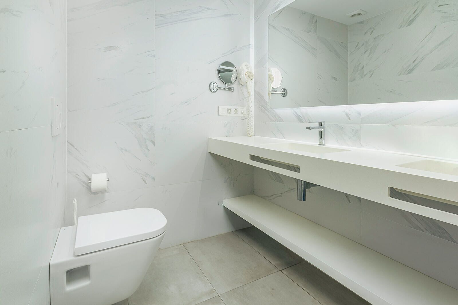 A bathroom with a white toilet, a sink with a mirror, and marble-patterned walls.